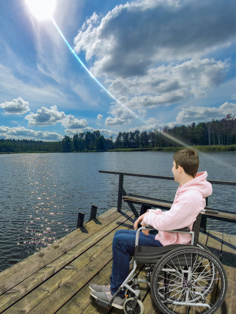 Teen in wheelchair on lake pier looking out at the water.