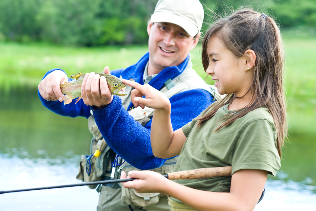 Angler holding fish while girl touches its head.